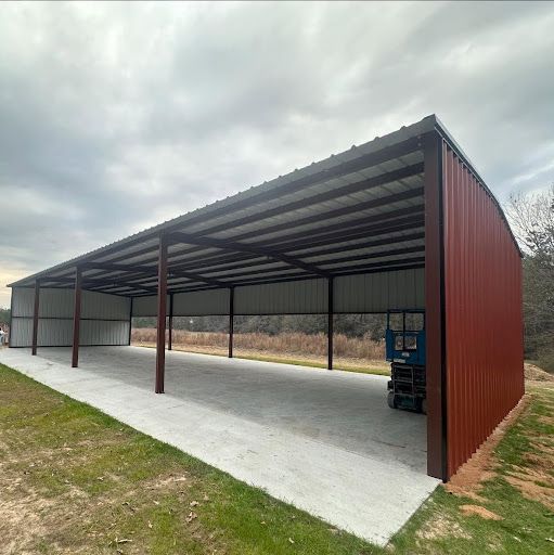 Open-sided red metal pole barn with a concrete floor